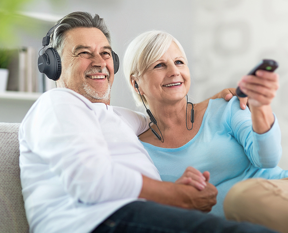 Elderly couple on the couch watching TV using the Avantree D4169 Bluetooth in-ear and over-ear headphones and transmitter