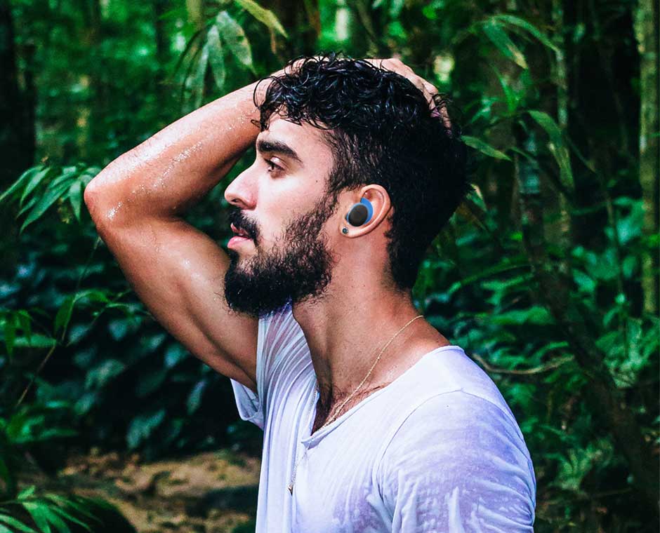 A man in the woods, sweating, wearing headphones, looking relaxed.